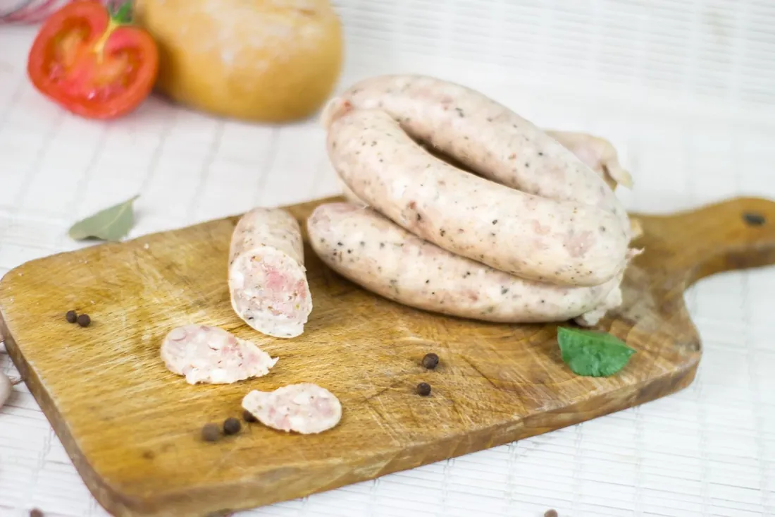 Fresh, coarse-cut sausages coiled on a wooden board with peppercorns and a bay leaf.