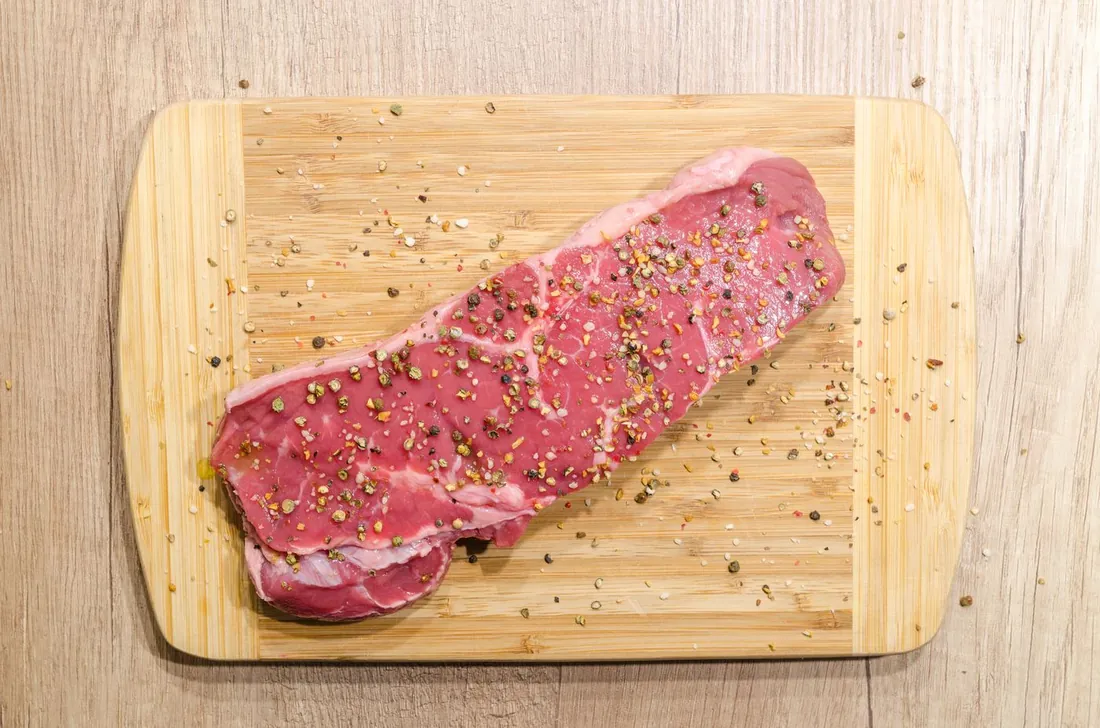 A thick sirloin steak, seasoned with cracked peppercorns, resting on a wooden chopping board.